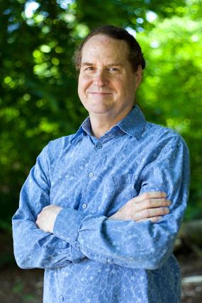 Geoff Korf stands in a blue shirt in front of trees