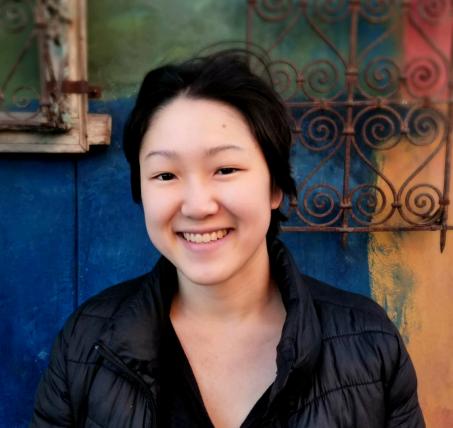 Malie sits in front of a multicolored background in a black shirt