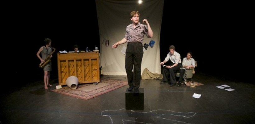 A man stands on a box over the chalk outline. Two men sit to the right, a saxiphonist and pianist are to the left.
