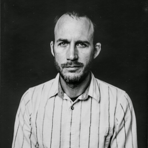 a man in a striped shirt standing in front of a dark background