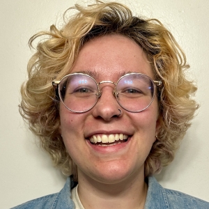 a blonde person with glasses smiling