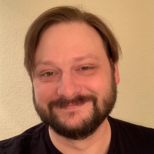 a brunette man smiling against a tan background