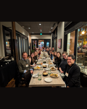 A group of UW Drama faculty, students, and alumni gathered around a long dinner table at a restaurant in Denver, smiling and celebrating their participation in the 2025 ASTR Conference. 