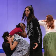 In the play "Everybody," an actor wearing a skeleton suit shouts while other characters cover their ears with their hands. 