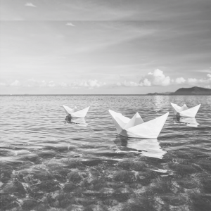 Black and white image of three paper boats on water