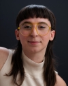 a brunette woman with glasses smiling against a dark bakground