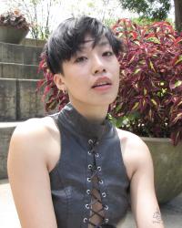 a light skinned Chinese-American nonbinary person with short black hair sitting in front of concrete steps and plants.