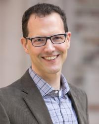 Scott smiling at camera, wearing glasses and blazer