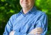 Geoff Korf stands in a blue shirt in front of trees