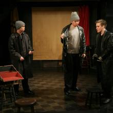 MacHeath talks with two of the henchmen, who areholding a bat and keys.