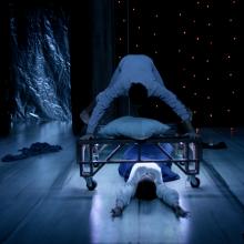 A man is on the table on his hands and feet while a woman flows under it.