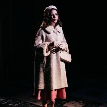 Woman in coat on stage.