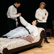 Ada and the Engine / Photo by Logan Guerrero Woman on feinting couch with man and woman standing over her