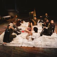 Actors sit on a blanket on the floor