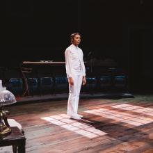Young women dressed in a white suit stands in a pool of light.