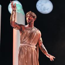 Actor in toga stands onstage with moon in background