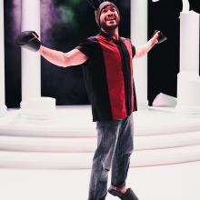 Actor dressed as bottom stands with his arms wide on stage.