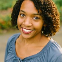 a woman with curly brown hair and a blue shirt smiling