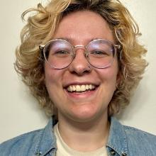 a blonde person with glasses smiling