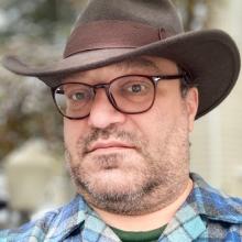 a man in glasses and a hat in front of a blurred background