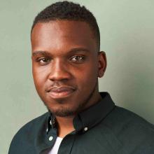 African-American male in a dark green button-up shirt against a mint green background with a soft smile at the camera.