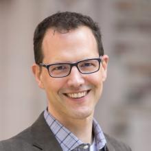 Scott smiling at camera, wearing glasses and blazer