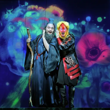 A person in a garment holding a stick next to a person in a garment.