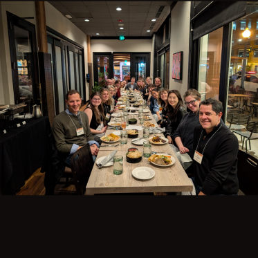 A group of UW Drama faculty, students, and alumni gathered around a long dinner table at a restaurant in Denver, smiling and celebrating their participation in the 2025 ASTR Conference.